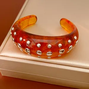 Detailopname van barnsteenkleurige hars armband met zilveren studs op doosje