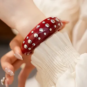 Detailopname van een rode hars open armband met ronde zilveren metalen studs versiering