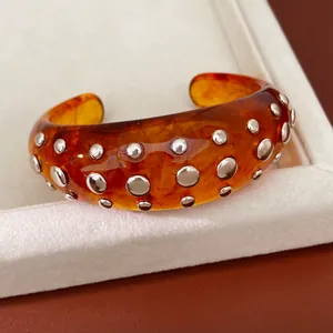 Detailopname van een amberkleurige hars armband met zilveren ronde studs