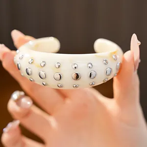 Detailweergave van een crème hars manchetarmband met gepolijste zilveren ronde studs.