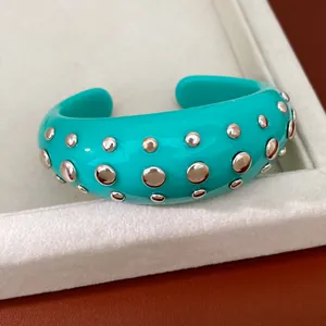 Close-up van turquoise hars manchetarmband met zilveren klinknagels en open ontwerp.