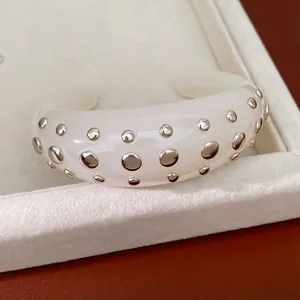 Close-up van een crèmewitte harsmanchetarmband met gepolijste zilveren ronde studs