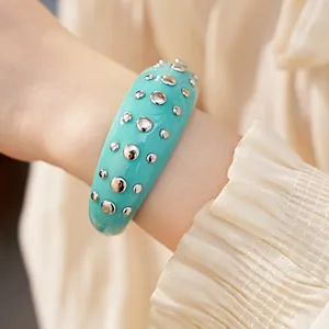 Close-up van een stijlvolle groenblauwe hars armband met zilveren klinknagels aan de pols