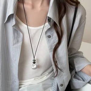 Detail of a minimalist silver teardrop necklace on a model wearing a striped shirt