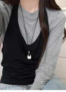 Close-up detail of a minimalist silver teardrop necklace on a stylish black and grey outfit.