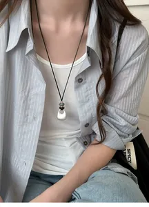 Close-up of a minimalist silver teardrop pendant necklace worn on a casual striped shirt