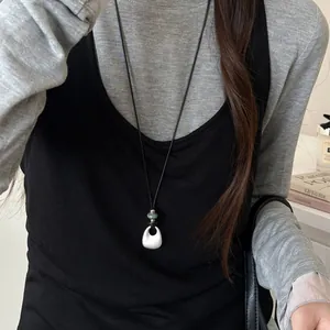 Minimalist long silver teardrop pendant necklace worn over black and grey layers.
