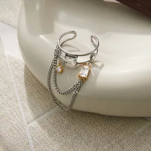 Detailansicht eines C-förmigen Edelstahlrings mit Zirkonia und hängenden Kettenelementen.