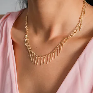 Elegant gold tassel necklace with textured copper bars worn with a stylish pink dress