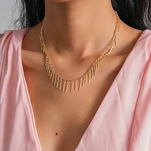 Detail of a vintage gold-finished necklace with elegant metal rod tassels on a pink top.