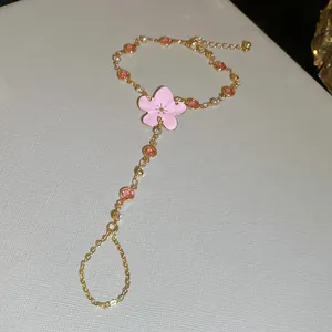 Elegante pulsera de mano dorada con una delicada flor de cerezo rosa y cristales