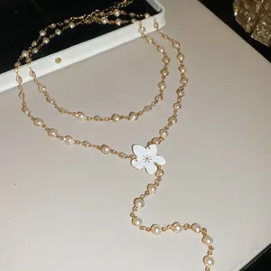 Detalle de un collar de cadena de metal dorado con perlas y un colgante de flor blanca