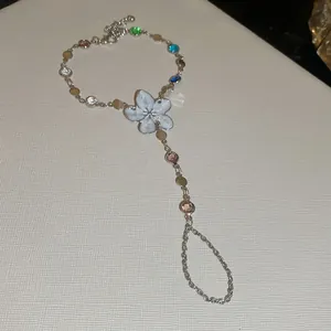 Vista detallada de una pulsera de mano plateada con flor de esmalte blanco y cristales de colores