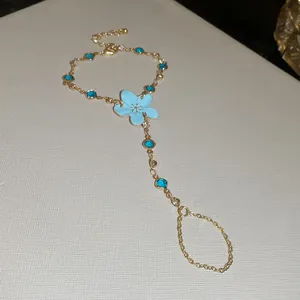 Vista detallada de una pulsera de mano dorada con flor de esmalte azul claro y cristales.