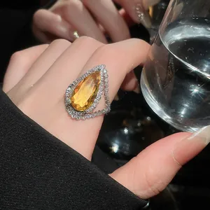Detailed shot of a pear-cut yellow gemstone ring with a double diamond halo on a finger