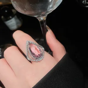 Close-up of a pear-cut pink gemstone ring with sparkling diamond halo on finger