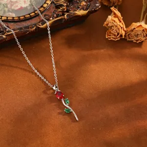 Collier pendentif tulipe argentée avec pierres rouges et vertes sur fond marron vintage