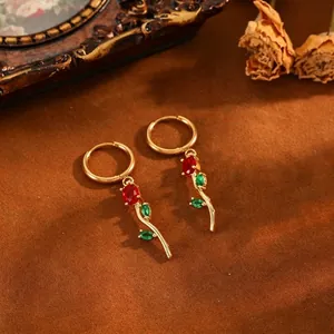 Macro detail of elegant gold tulip hoop earrings featuring red and green gemstones