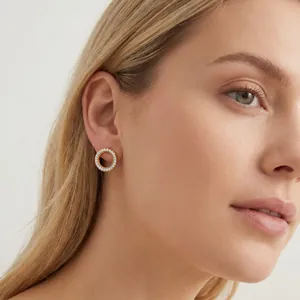 Close-up van goudkleurige holle cirkeloorbellen met fonkelende kristallen op een model.