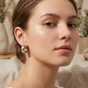 Detailed view of a silver stainless steel chunky hoop earring on a model's ear.