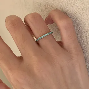 Close-up view of a minimalist eternity ring with turquoise blue stones on a finger