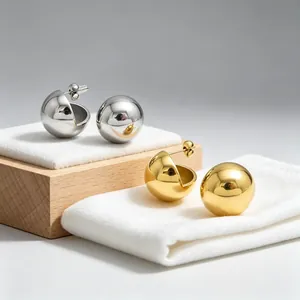 Detail view of gold and silver minimalist stainless steel ball earrings on white fabric.