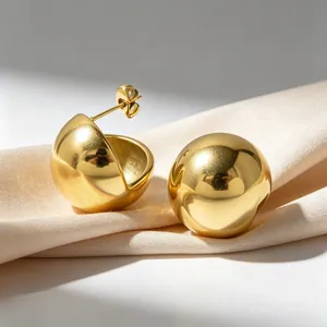 Macro view of polished gold stainless steel hemispherical stud earrings on beige silk fabric