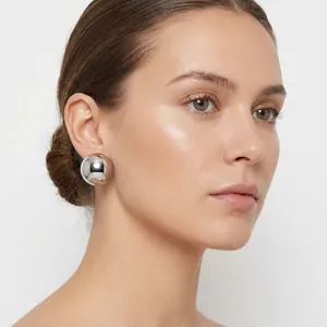 Detail of a minimalist silver stainless steel half-ball stud earring on a model.