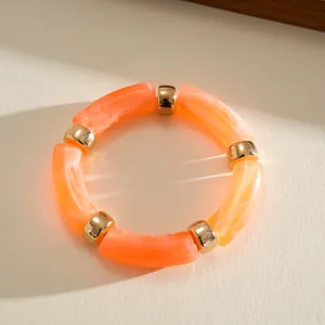 Dettaglio di perle cilindriche in acrilico marmorizzato arancione con distanziatori dorati.
