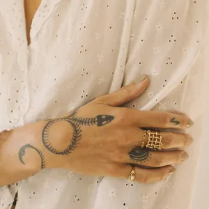Close-up of gold-plated woven geometric ring on tattooed hand with white blouse.