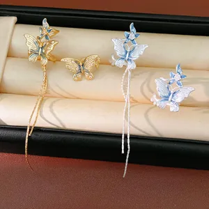 Dettaglio degli orecchini a farfalla asimmetrici con nappe in smalto blu e zirconi.