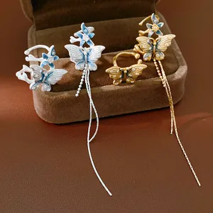 Dettaglio di orecchini a farfalla asimmetrici con lunghe nappe e zirconi brillanti