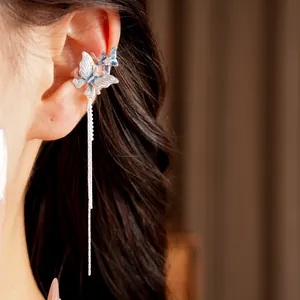 Primo piano di un ear cuff asimmetrico con nappa, farfalla blu e dettagli in smalto