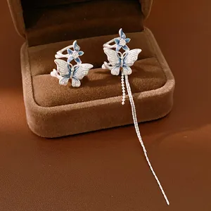 Dettaglio di orecchini a clip a farfalla asimmetrici con smalto blu e nappa lunga d'argento
