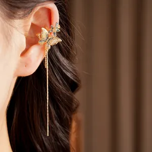 Dettaglio macro di un elegante ear cuff dorato con farfalla e una lunga nappa pendente