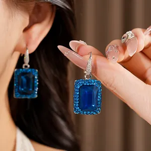 Close-up of elegant square blue gemstone earrings with rhinestone halo detail