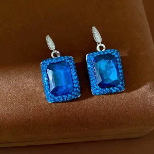 Close-up view of elegant square blue gemstone earrings with blue rhinestone halo.