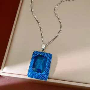 Close-up of square blue gemstone pendant with rhinestone border on silver chain