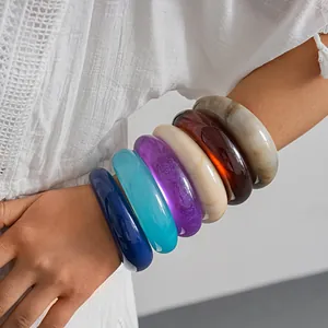 Detailed view of six chunky colorful marbled resin round bangles on a woman's arm