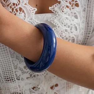 Close-up shot of a glossy deep blue resin bangle bracelet worn with white lace garment
