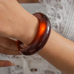 Detailed close-up of a vintage translucent amber-brown resin bangle on a lace-sleeved arm