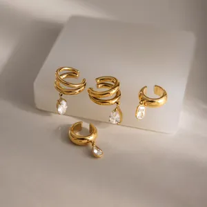Detalle de brazaletes de oreja dorados de acero con colgantes de gemas claras.