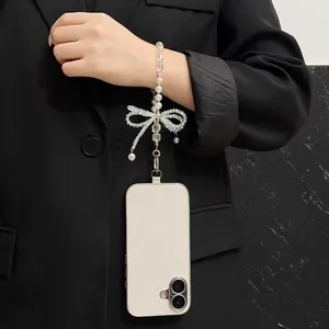 Detalle de una correa de perlas para móvil con lazo en una funda con purpurina.