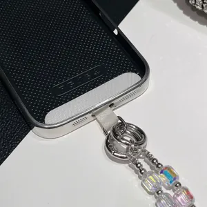 Detalle de correa de teléfono con cuentas de colores, anillos metálicos y junta de fijación.
