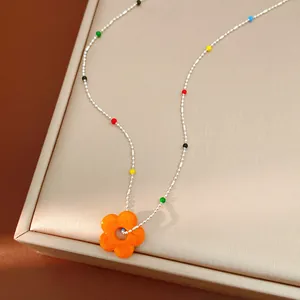 Détail en gros plan d'un collier de fleurs en verre dopamine sur un support beige.