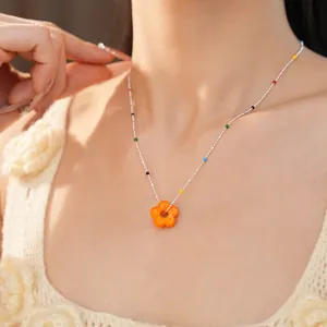 Vue détaillée d'un collier avec pendentif fleur en verre orange porté par un modèle.