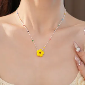 Détail d'un collier avec pendentif fleur en verre coloré porté sur le cou d'un modèle