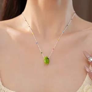 Gros plan d'un collier fleur en verre coloré sur la clavicule d'un mannequin.