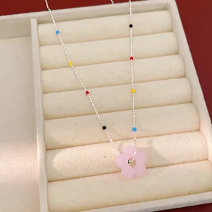 Gros plan d'un collier de style doux avec une fleur en verre rose et des perles colorées