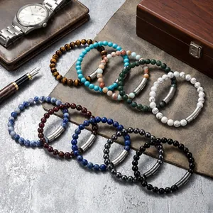 Dettaglio di bracciali in perle di pietra naturale su pelle con orologio di lusso e penna.